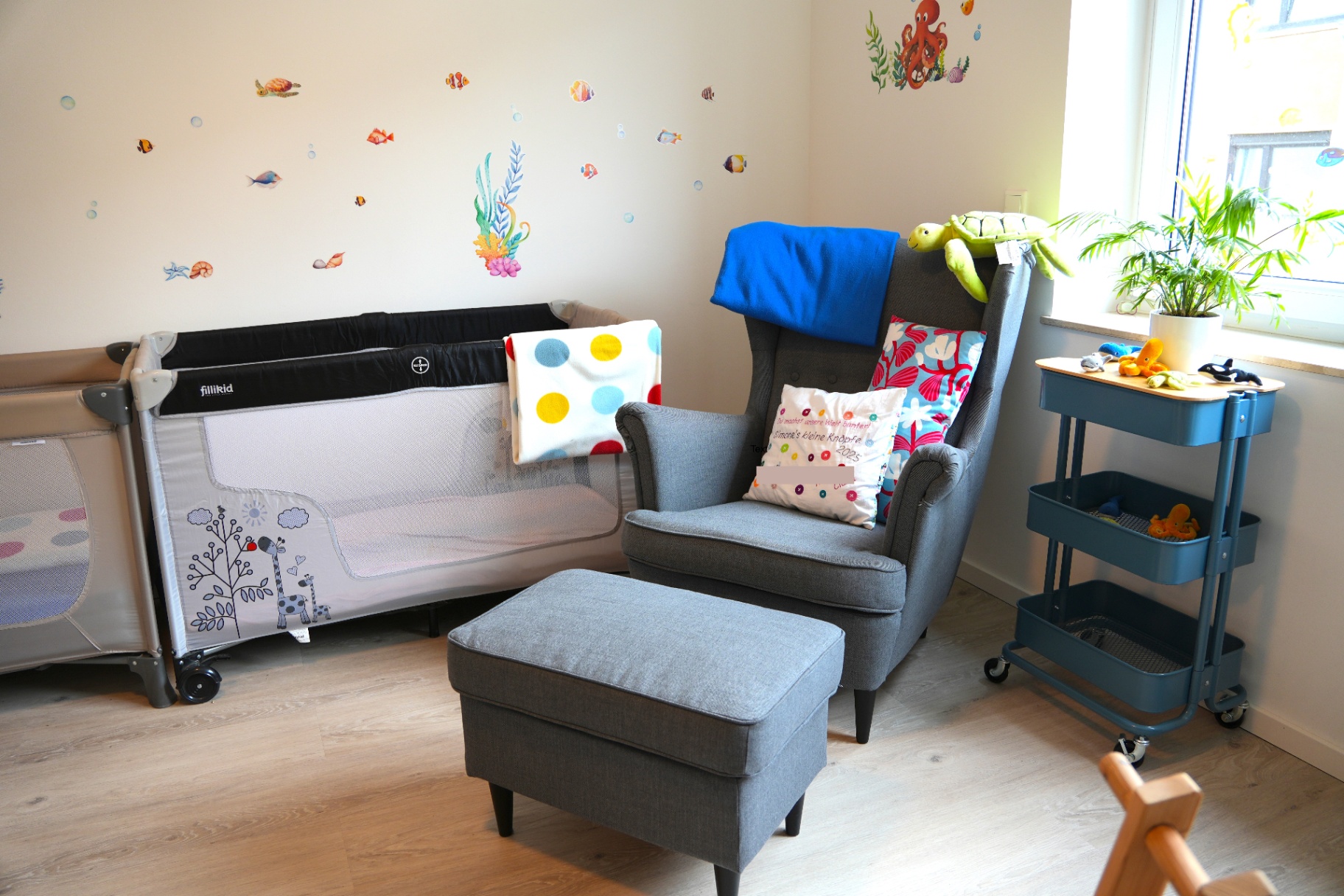 Gemütlicher Lesesessel neben Babybett und Spielwagen